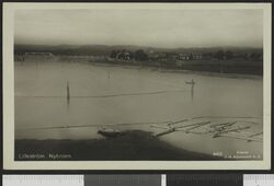 Utsikt fra Rælingen mot Nitelva med Nybrua i bakgrunnen. Lillestrøm ligger til høyre. Bildet er hentet fra Nasjonalbibliotekets bildesamling.