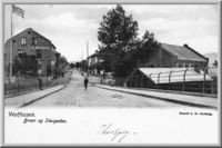 Storgata i Vestfossen på begynnelsen av 1900-tallet sett fra brua. Bildet er manipulert, med flagg og bokstaver på kjøpmann L.G.Nedbergs gård.