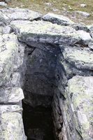 Detalj frå fangstgrop 1 i fangstanlegg 4. Merk korleis steinhellene i enden av gropa er lagt opp: på høgkant slik at dei skarpe klovane på fanga dyr ikkje skulle få feste til å kome seg opp. I øvste kant er ei helle lagt med utstikk av same grunn. Foto: Arnfinn Kjelland (2014)