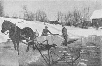ISLASTING PÅ SCHWATRZEDAMMEN 1912-25. To mann laster isblokker på hesteslede/slådd for transport fra Schwartzedammen til lagring eller lasteplass. Isen fra Schwartzedammen som skulle lagres ble det første stykket fraktet med hest og slådd. Deretter sendt i Isrenne ned til isstabelen på Graffodden eller på Faltstranda. Søndre Nærsnes gård i bakgrunnen (Foto fra Killingstad; Røyken bygd før og nu 1928, fotograf ukjent)