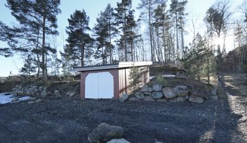 Båthuset er bygd inn i muren som dannet den nederste av isstablene på Graffodden. Bak det røde båthuset ser vi grunnmuren til den midterste stabelen, der kyststien passerer over. (Foto: Victor Iversen 2021) .