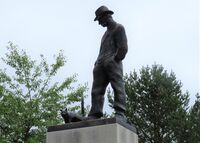 Motivet "Mannen med katten" fra Skredsvigs maleri "Idyll" er gjenskapt som skulptur, utført av Nils Aas, avduket i sentrum av Eggedal i 2004. Foto: Stig Rune Pedersen (2021)