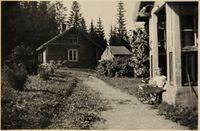 "Gamlestua" på Mathisrud Midtre til venstre. Ingrid Jemtland (Knapp) sitter på trappa til våningshuset. Foto: ukjent (familien Jemtland)