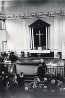 Alterpartiet i Moland kyrkje ein gong mellom 1908 då det vart måla girlander og 1937 då det vart innlagd elektrisitet. På sokkelen står: "Det er fullenda". Vi ser ei enkel parafinlampe frå taket. Det ser ut til å vere ein visitas med overhøyring. Fotograf er Olav S. Nylid