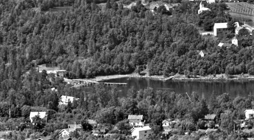 NÆRSNESBUKTA 1958. Den siste isstabelen lå på Flatstranda. Siste året det ble lagret is var 1960. "Den store isbrygga" ble ikke brukt de siste årene, men all isen som ble solgt ble lastet fra "den lille isbrygga" på landsiden av bukta, mot kirken. Bildet er et utsnitt av et større flyfoto over Nærsnes (Foto Widerøe. Samling; Nasjonalbiblioteket )