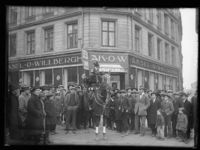 En gruppe menn og gutter samlet utenfor slakterforretningen. Trolig fra åpningen av forretningens nye lokaler i 1923. Foto: Narve Skarpmoen, Nasjonalbiblioteket.