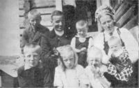 Bilete 6: Anne og Ole med seks av ungane på trappa utanfor Osestølen, og den sjuande, Torleiv, moglegvis i døra. Familien er pynta til fest. Biletet kan vera frå dåpsdagen til Sissel, som vart fødd i januar 1925. Ukjent fotograf, 1925.