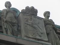 Lars Utne sin skulpturgruppe «Arbeid og fred» i kleberstein fra 1906 over inngangspartiet på daværende Norges Bank, Bankplassen 4 i Oslo. Mellom figurene er riksvåpenet. Foto: Stig Rune Pedersen (2012)