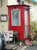 Telefonkiosk i tre, på verftstomta til Kaarbøs Mek. Verksted i Harstad, malt i samme farge som oroginalen og er ellers en tro kopi av den originale Telenor-kiosken som arkitekt Georg Fredrik Fasting tegnet i 1932. Den ble bygd på dugnad av verftsarbeiderne - slik at de skulle slippe å gå opp på et av kontorene for å ringe ut eller motta beskjeder. Foto: Gunnar E. Kristiansen (2016).