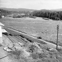 Foto tatt fra tatt fra loftsvinduet 1959, her ser vi det jobbes på jordet med hest. I bakgrunnen ligger Skårerødegården hvor skihallen SNØ kom på plass i 2020.